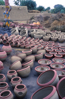 Pots Ready for Firing ||| Firings take place every Saturday and Sunday. By mid-afternoon, the unfired pots are brought to the firing place. This takes many hours. For each trip to the firing place, a woman carries at least two on her head and one in her hand. Visible here are pots for storing water, cooking, carrying embers, and wavy lipped flower pots.